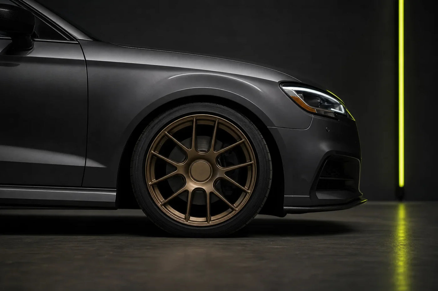 Bronze alloy wheel positioned naturally inside the front fender of a graphite performance sedan